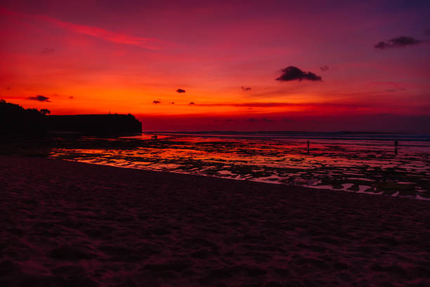 Ocean beach with waves and reflection at bright sunset or sunrise in Bali.