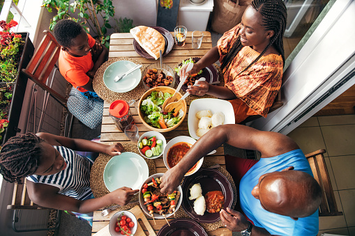 overhead view on family having dinner with barbecue, vegetarian skewers and traditional african food on balcony