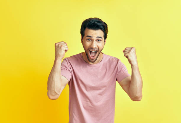 istock Happy man celebrating his success with winner gesture on yellow background. 1265200726