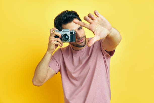 istock Handsome man taking photo with retro camera on yellow background 1265200731