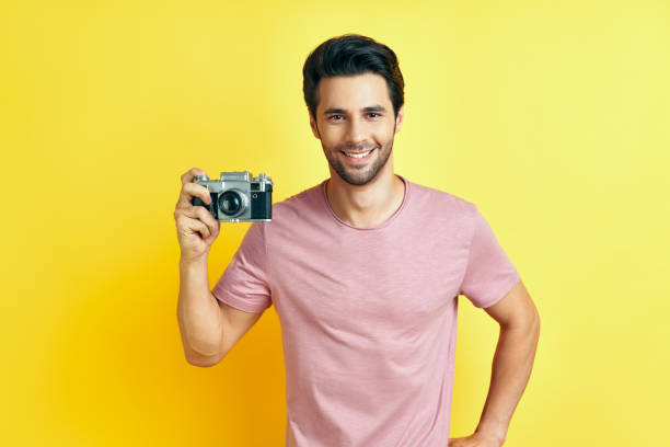 istock Smiling handsome man with retro camera on yellow background 1265200732