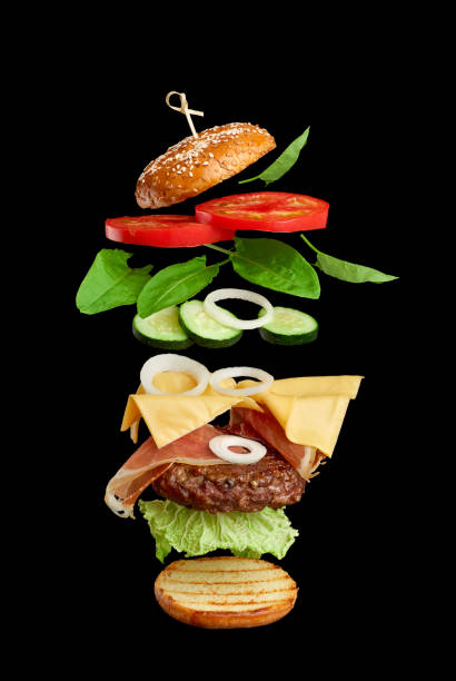 istock flying burger ingredients: cutlet, sesame seed bun, tomato, onion, green lettuce, cheese on black background 1265201532