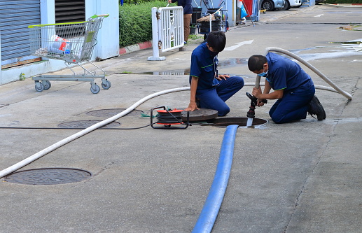 Bangkok, Thailand- August 11, 2020: A worker uses water hose injecting high pressure water into sewer for cleaning process