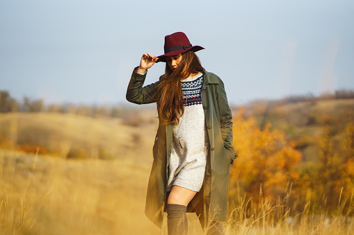 Beautiful young stylish woman in a coat walks in the autumn in the park. The girl is dressed in a green coat and a red hat. Beautiful evening. Autumn fashion. Lifestyle. High fashion portrait.