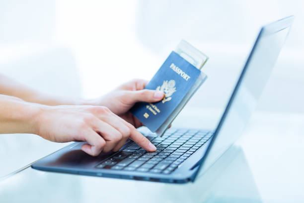노트북 컴퓨터를 사용하는 동안 돈이 있는 미국 여권을 들고 있는 남성의 손. 온라인 여행 예약. - passport passport stamp usa travel 뉴스 사진 이미지