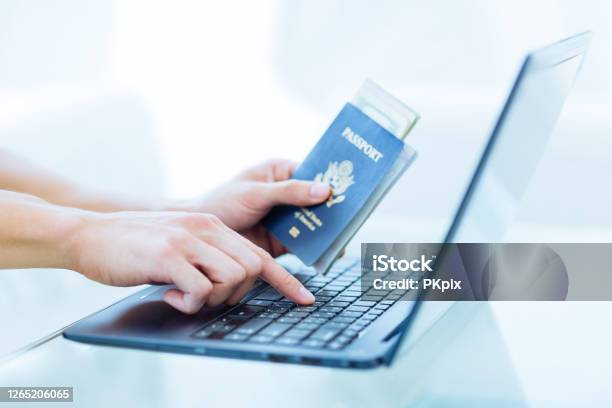 Male Persons Hands Holding A Us Passport With Money While Using A Laptop Computer Online Travel Booking Stock Photo - Download Image Now