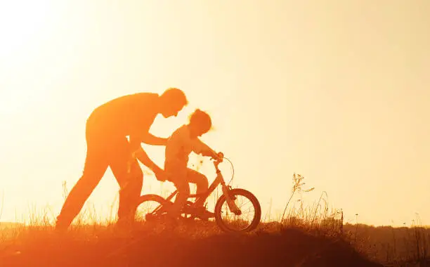 Photo of Silhouette of father teaching his daughter to ride a bike at sunset