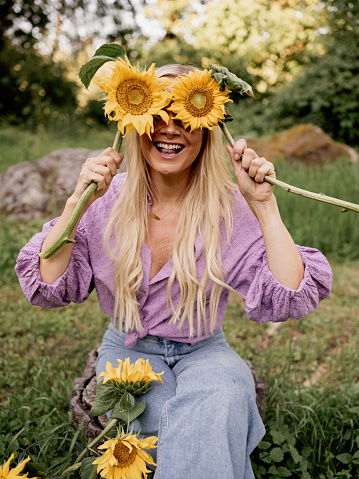 Woman with sunflowers in her hand fun and summer cute\nPhoto taken outdoors in summer in natural light woman hiding behind sunflowers