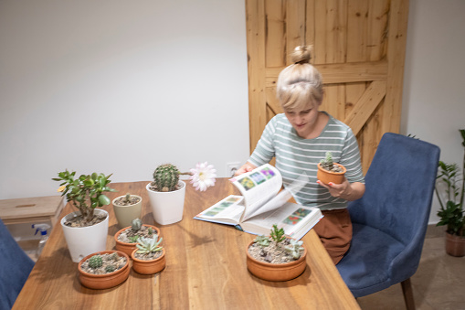 Beautiful, young woman learning from the encyclopedia about planting succulent plants at home.