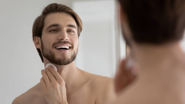 istock Close up mirror reflection overjoyed young man applying aftershave lotion 1265210571