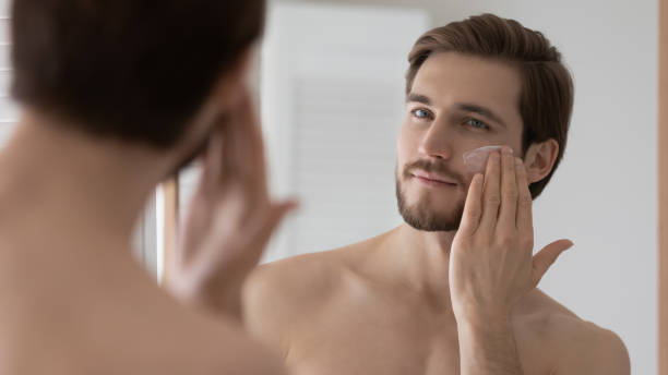 istock Close up mirror reflection handsome young man applying moisturizing cream 1265210600