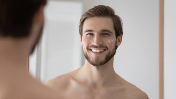 istock Head shot mirror reflection smiling young man applying moisturizing cream 1265210604