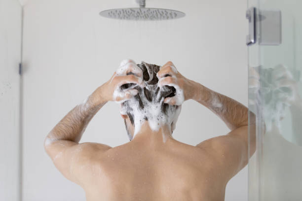 Rear view young man washing hair, standing in bathroom Rear view young man cleaning hair with foamy anti dandruff shampoo close up, standing in modern bathroom at home, taking morning shower, washing head and body, personal hygiene and skincare concept dandruff men stock pictures, royalty-free photos & images