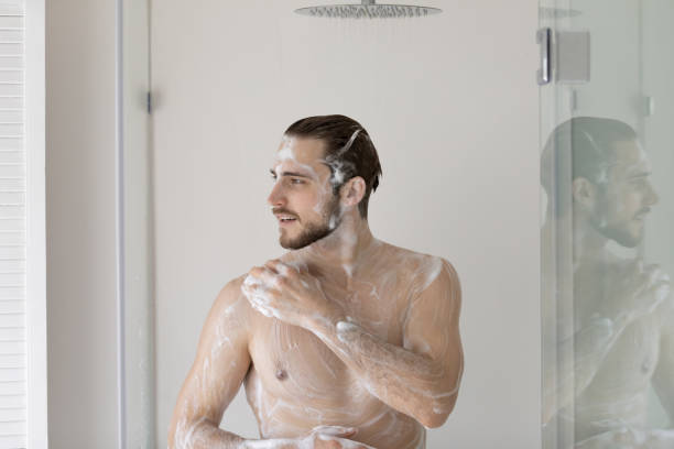smiling young man standing in bathroom, taking shower - soap body imagens e fotografias de stock