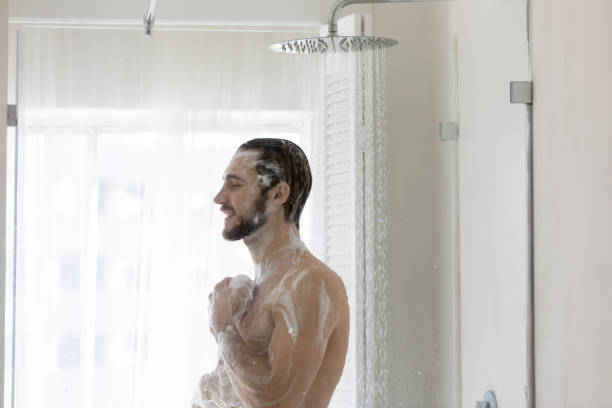 Smiling young man taking morning shower, standing in modern bathroom Smiling young man taking morning shower, standing in modern bathroom, applying natural moisturizing foamy gel or shampoo, holding fluffy bath puff, personal hygiene and skincare concept shower gel stock pictures, royalty-free photos & images