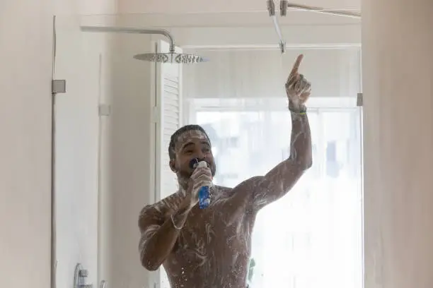Photo of Positive African American man having fun in bathroom, singing