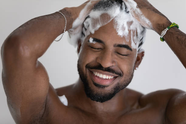 Close up smiling African American man washing hair with shampoo Close up smiling African American handsome young man washing cleaning hair with foamy anti-dandruff shampoo, taking shower, enjoying morning routine procedure, standing in bathroom black male massage stock pictures, royalty-free photos & images
