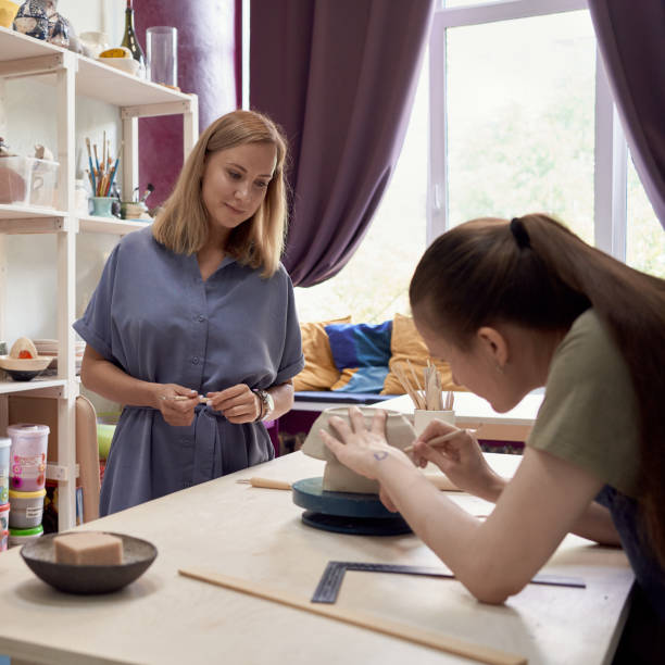 istock Female ceramic teacher looking at young apprentice doing pottery in workshop 1265212506