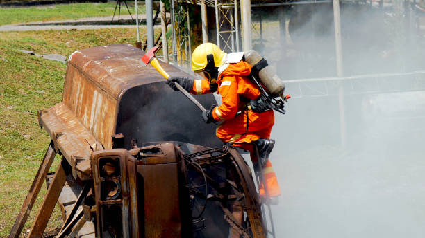 istock Firefighter fighting with flame using fire hose chemical water foam spray engine. Fireman wear hard hat, body safe suit uniform for protection. Rescue training in fire fighting extinguisher 1265213788