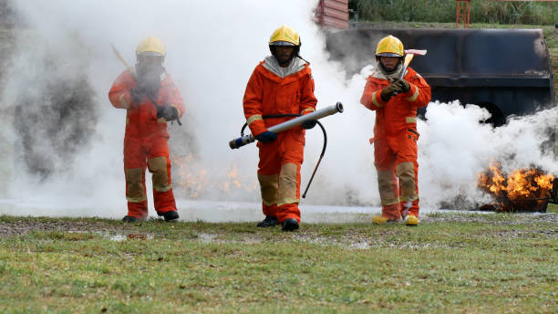 istock Firefighter fighting with flame using fire hose chemical water foam spray engine. Fireman wear hard hat, body safe suit uniform for protection. Rescue training in fire fighting extinguisher 1265213805