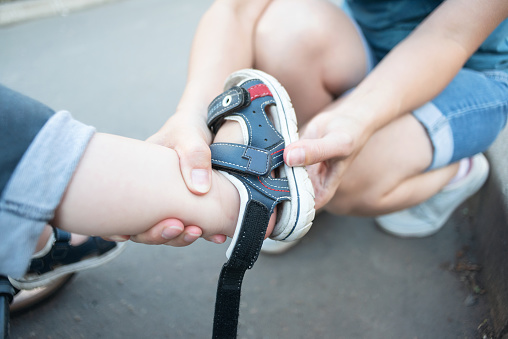 Mom puts sandals on the feet of the child close up.