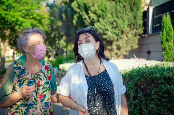 Caregiver and her client wear face protective masks while strolling during the coronavirus epidemic. stock photo