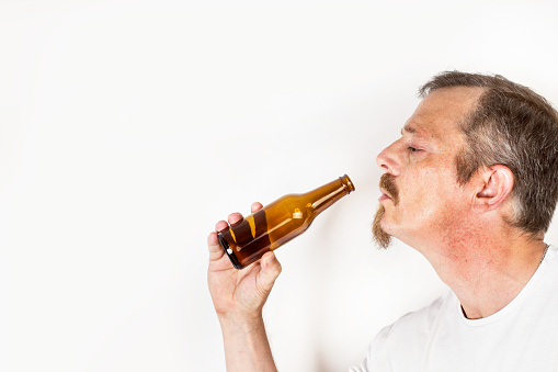 Man holding a bottle of beer in front of his mouth on a white background