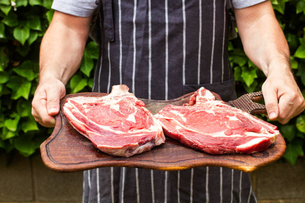 hombre sosteniendo una tabla de madera de cocina con dos filetes - veal meat raw steak fotografías e imágenes de stock