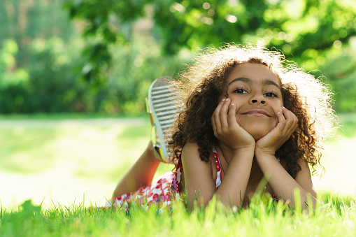 Portrait of cute black girl lying on a grass in a city park