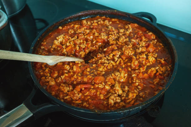 przygotowanie sosu bolonie w kuchni domowej - chude mięso z indyka w sosie pomidorowym na patelni na kuchence, z bliska. - simmered zdjęcia i obrazy z banku zdjęć