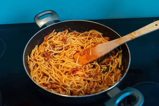 May 27, 2020 - Warsaw, Poland: Homemade spaghetti bolognese in a frying pan on a stove in a domestic kitchen - isolated view, close up, wooden spatula, messy.