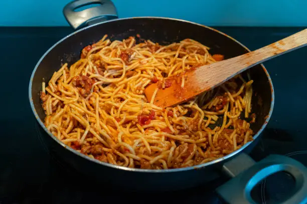 May 27, 2020 - Warsaw, Poland: Spaghetti pasta with bolognese meat sauce in a skillet on a stove - homemade Italian dish with fresh tomatoes, carrots, low calorie white meat and wholegrain spaghetti. for healthy eating.