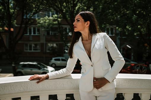 Beautiful young fashionable woman wearing a white suit outdoors at the balcony