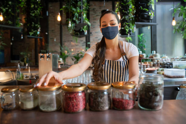 istock Waitress arranging jars on counter at the restaurant wearing a facemask 1265230982