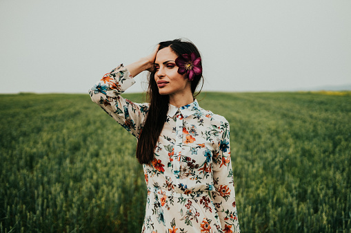 Beautiful young woman wearing long floral pattern dress in the agricultural field on a sunny summer day