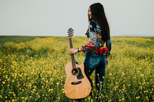 Beautiful young woman carrying a guitar on a sunny summer day in nature in the agricultural field