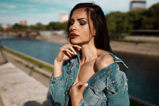 Portrait of a beautiful young woman wearing a denim jacket outdoors in the city street on a sunny summer day