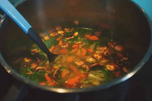 May 26, 2020 - Warsaw, Poland: Vegetable soup in a pot in domestic kitchen - preparing heathy vegan, vegetarian food with fresh carrots, mushrooms, parsley, potatoes.
