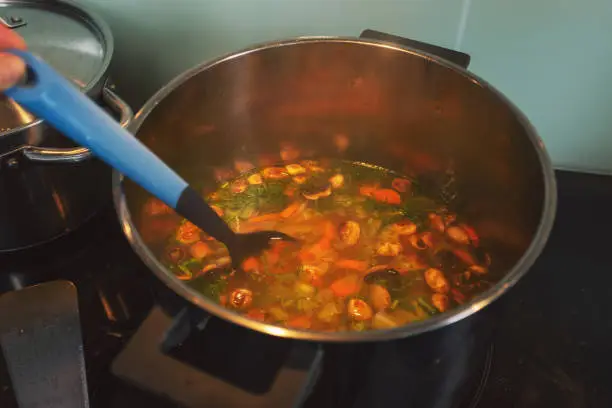 May 26, 2020 - Warsaw, Poland: preparing vegetable soup in domestic kitchen - steaming hot soup close up in a metal pot with a plastic soup for stirring