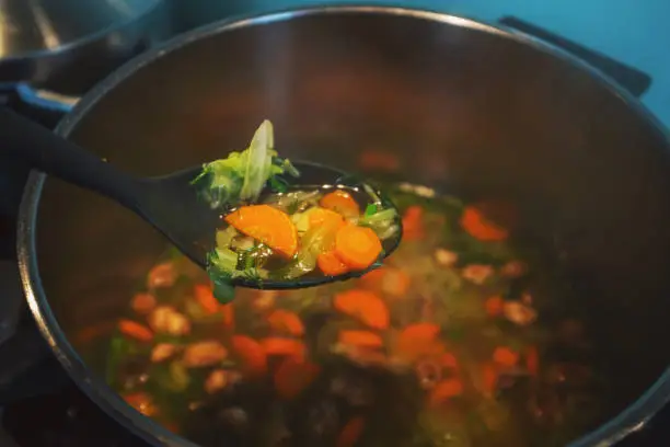 May 26, 2020 - Warsaw, Poland: vegetable soup in pot and plastic spoon - close up with carrots, cabbage, parsley, dill - vegan, vegetarian dish, healthy eating, extreme close up in domestic kitchen.