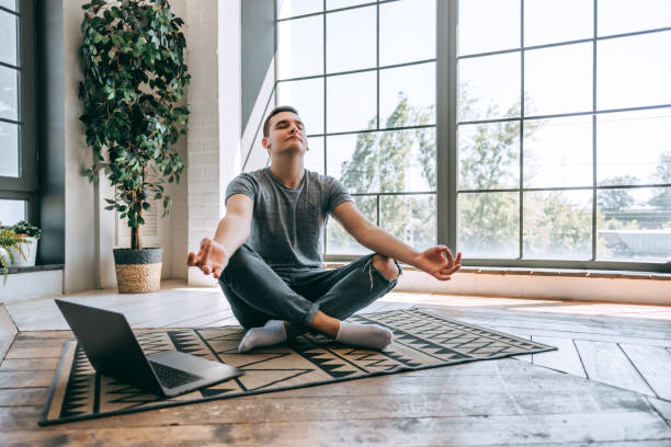 erfreuliche kaukasische entspannte student sitzt gekreuzte beine auf dem boden in der nähe geöffnet laptop - zen like meditating yoga business stock-fotos und bilder
