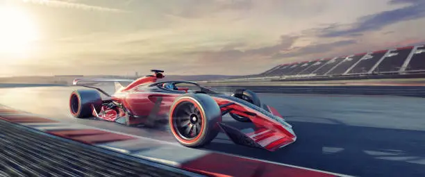 A close up wide angle image of a generic red, white and black racing car moving at high speed on the outer edge of the track just coming out of a corner. The car is racing at a generic location, with empty stands in the distance, at sunset or dawn.