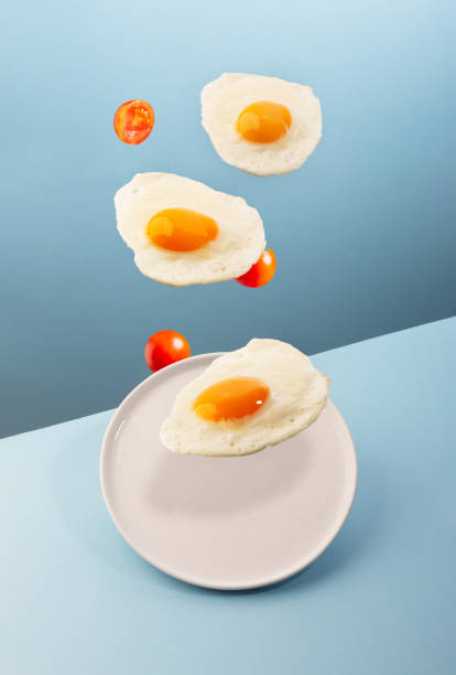 Three flying eggs and a plate on the modern blue background stock photo