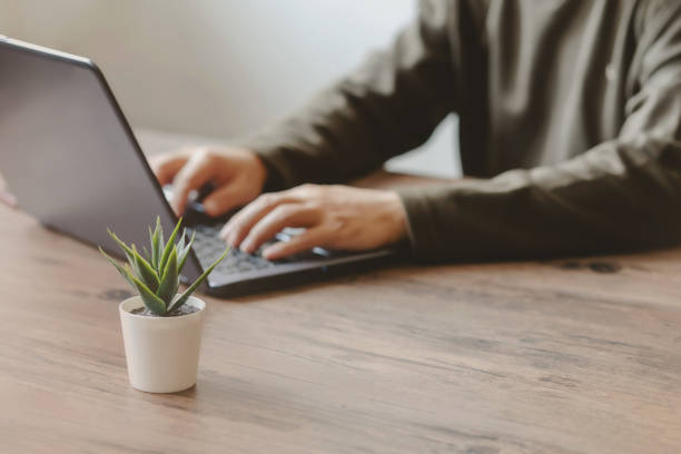 istock Man typing on a laptop keyboard on a wooden table and tree. 1265241177