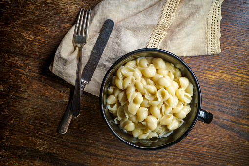 White cheddar shell macaroni and cheese on rustic wooden table with dark moody lighting
