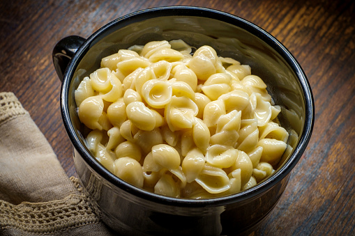 White cheddar shell macaroni and cheese on rustic wooden table with dark moody lighting