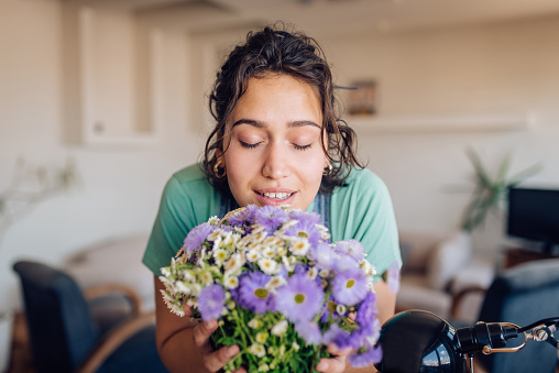 Portrait of a young woman smelling a fresh flower bouquet and enjoying at home.