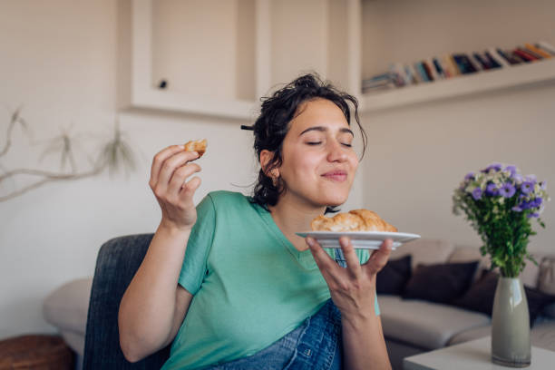 hermosa chica disfrutando del sabor de un croissant fresco - tasting women eating expressing positivity fotografías e imágenes de stock