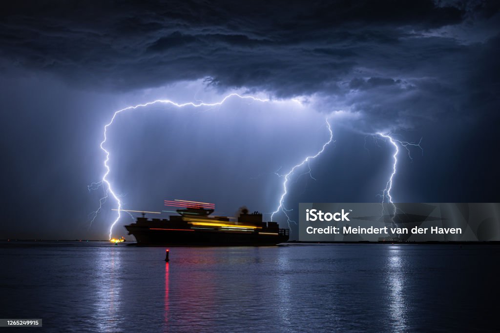 Sailing ship during a severe lightning storm Container ship is leaving the port of Antwerp during a severe thunderstorm. Light trails due to movement of the ship. Storm Stock Photo