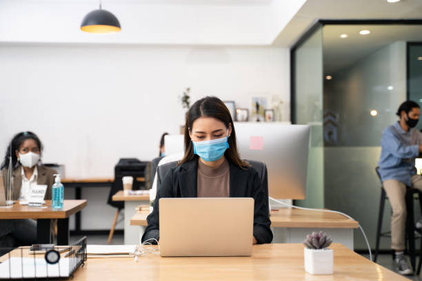 Asian young businesswoman working on computer in office with new normal lifestyle concept. Man and woman wear protective face mask and keep distancing to prevent covid virus after company reopen again Asian young businesswoman working on computer in office with new normal lifestyle concept. Man and woman wear protective face mask and keep distancing to prevent covid virus after company reopen again again stock pictures, royalty-free photos & images